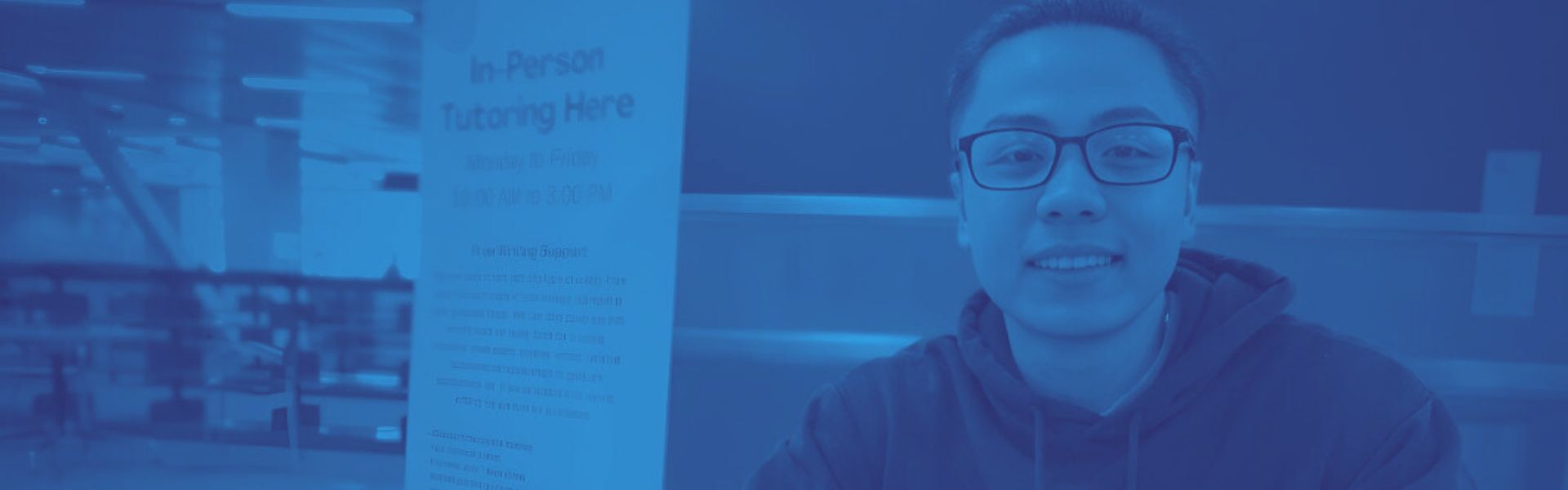 Writing tutor seated at rtable by banner with blue color overlay